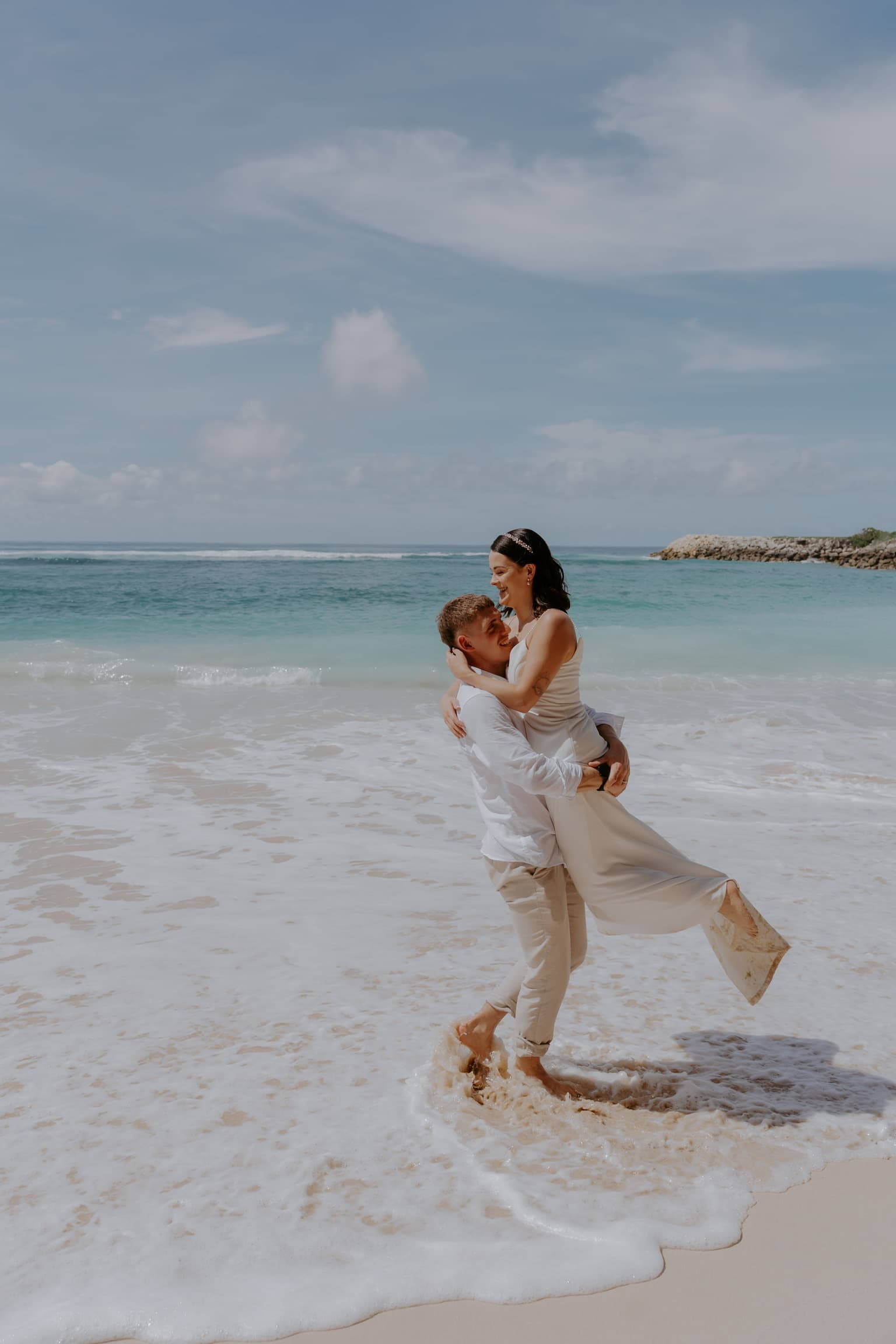 Clayton lifting Tamara in the ocean waves on a beach