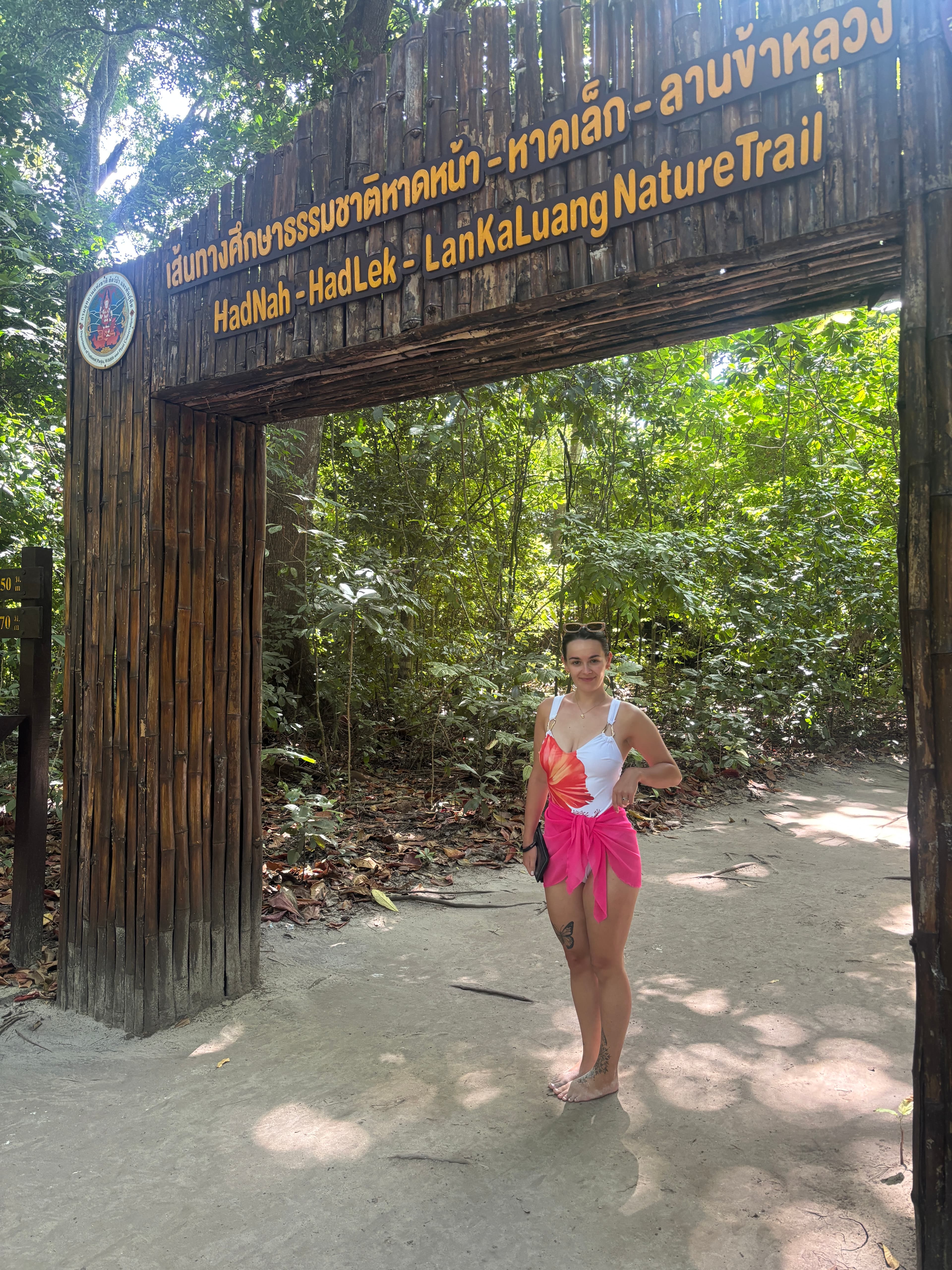 Tamara at a nature trail entrance in a swimsuit and pink sarong